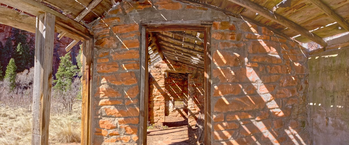 A stone building with a wooden roof structure, surrounded by dry grass and trees.