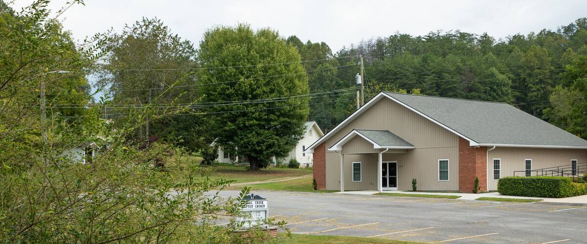 A church building with a parking lot and surrounding greenery.
