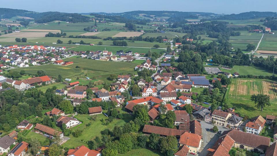 A rural village with red-roofed houses, green fields, and solar panels.