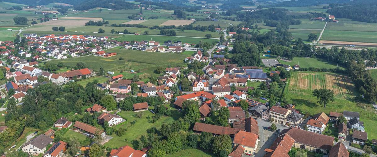 A rural village with red-roofed houses, green fields, and solar panels.