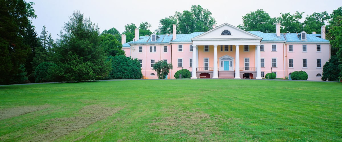 A large pink building with a blue roof, surrounded by a well-maintained lawn and dense trees.