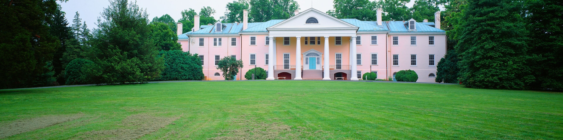 A large pink building with a blue roof, surrounded by a well-maintained lawn and dense trees.