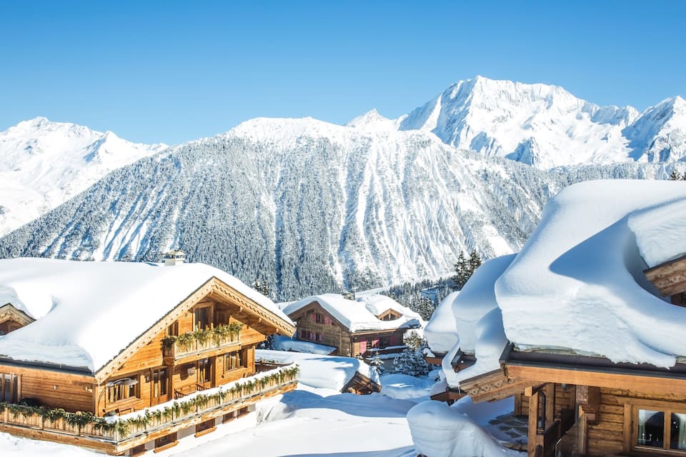 Un village de montagne enneigé, avec des maisons en bois et un ciel d’un bleu limpide.