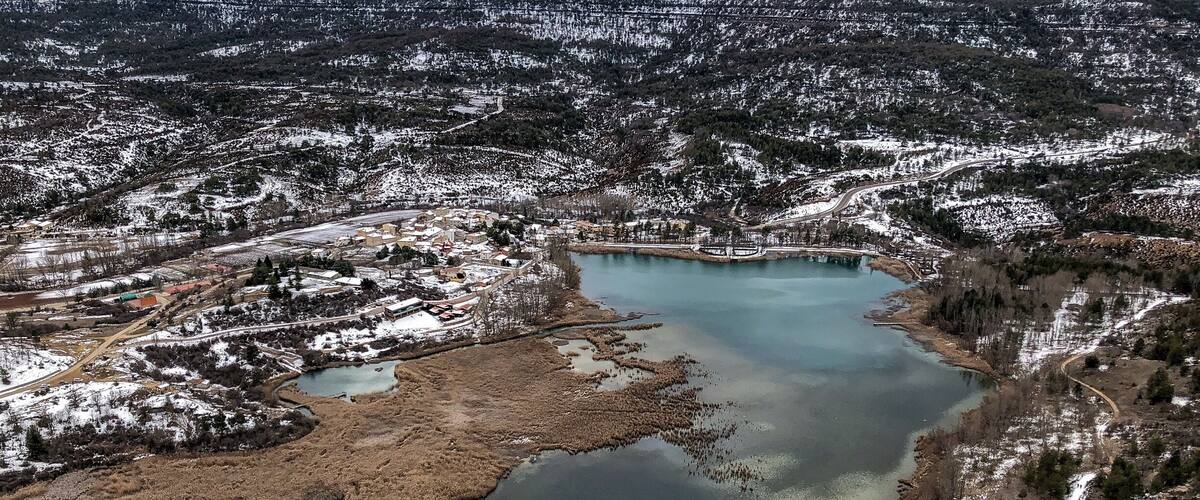 A snow-covered landscape with a large lake surrounded by trees and buildings.