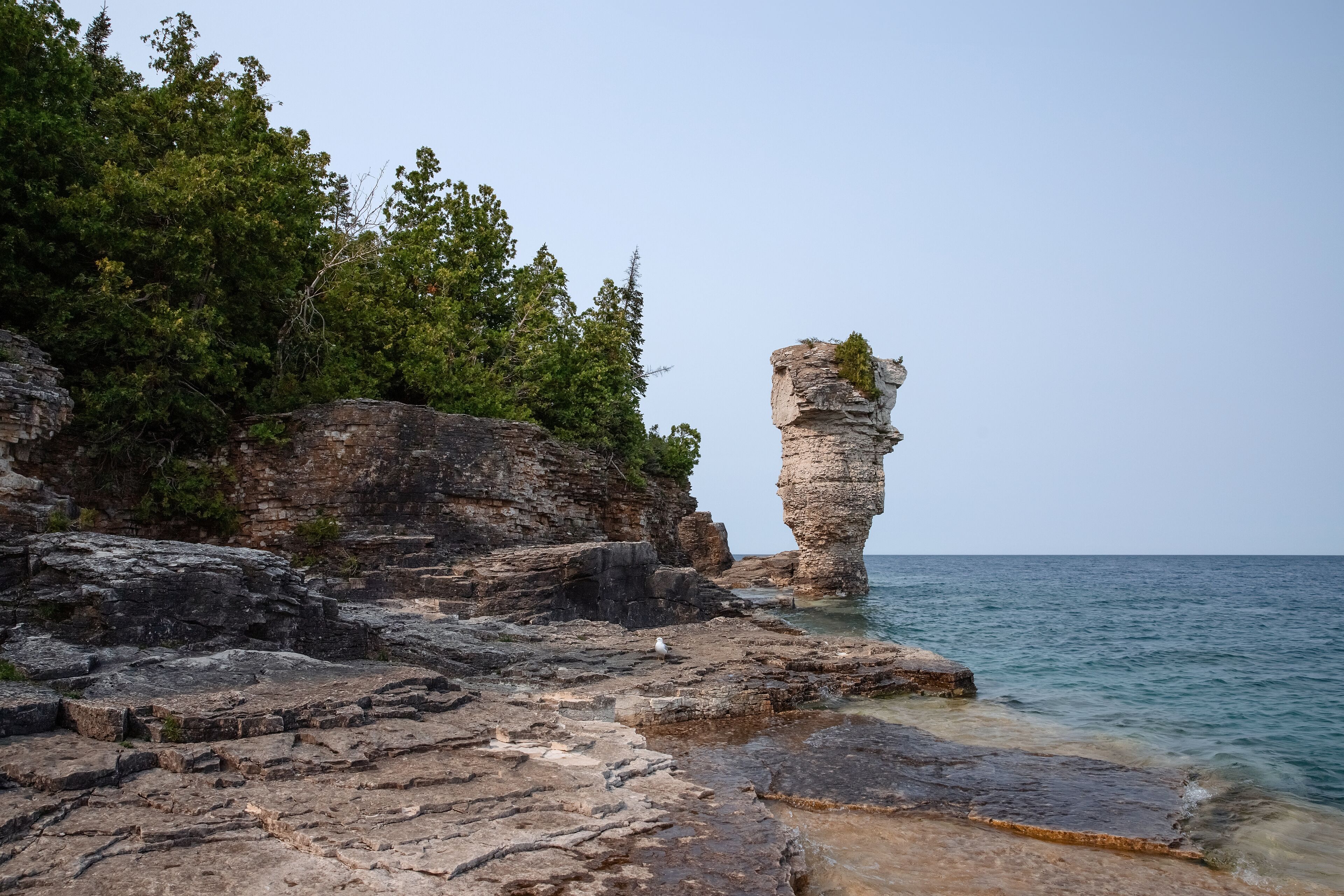 A coastal landscape with a prominent rock formation and a clear view of the sea.