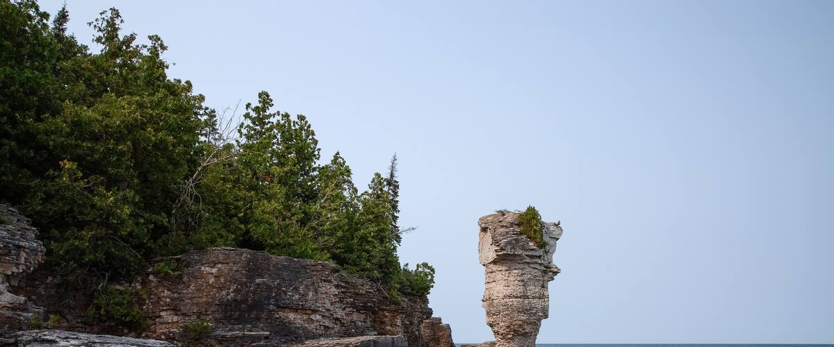 A coastal landscape with a prominent rock formation and a clear view of the sea.