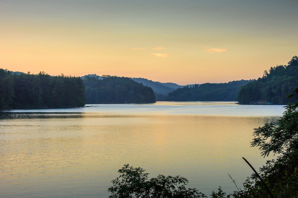 Ein ruhiger See, umgeben von dichten Wäldern, während der Sonnenuntergang stattfindet.