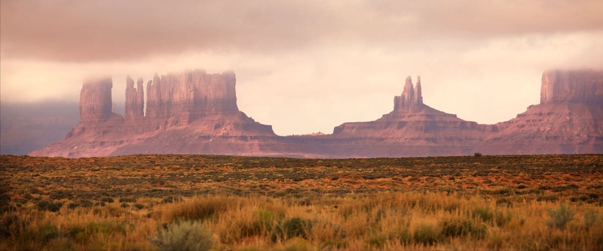 A desert landscape with prominent rock formations in the distance under a cloudy sky.