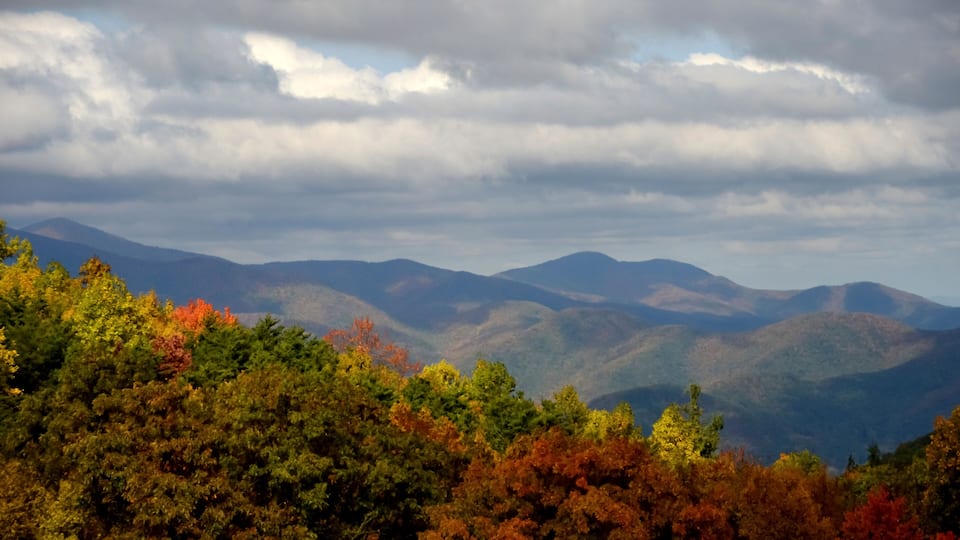 A mountainous landscape with autumn foliage and a cloudy sky.