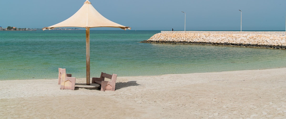 A beach with a sandy shore, a concrete pier, and a large umbrella providing shade.