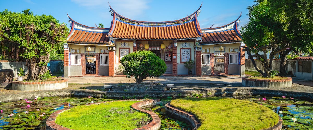 A traditional Chinese building with a curved roof and a pond with lotus flowers.