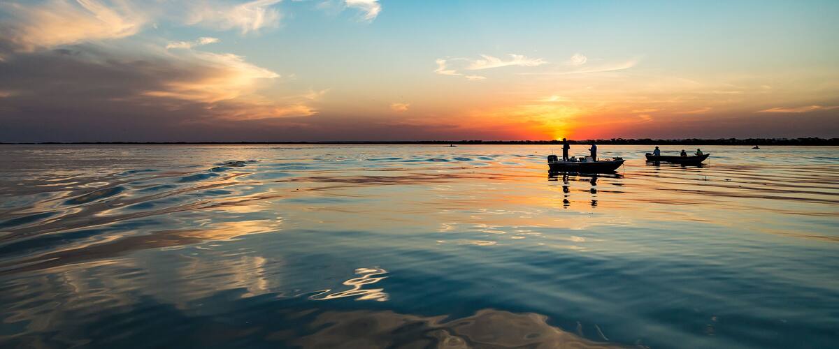 A calm lake at sunset with boats and people on the water.
