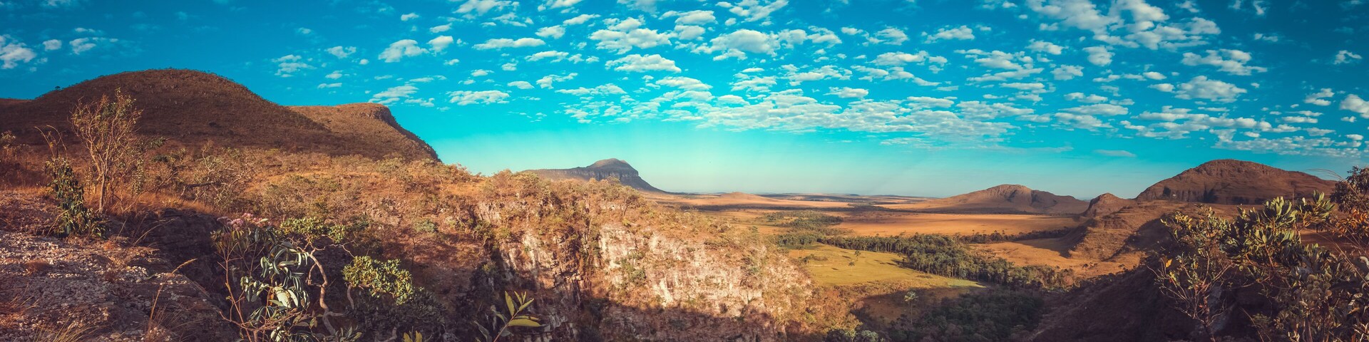 Un paisaje agreste con colinas ondulantes, vegetación escasa y un cielo azul despejado con nubes dispersas.