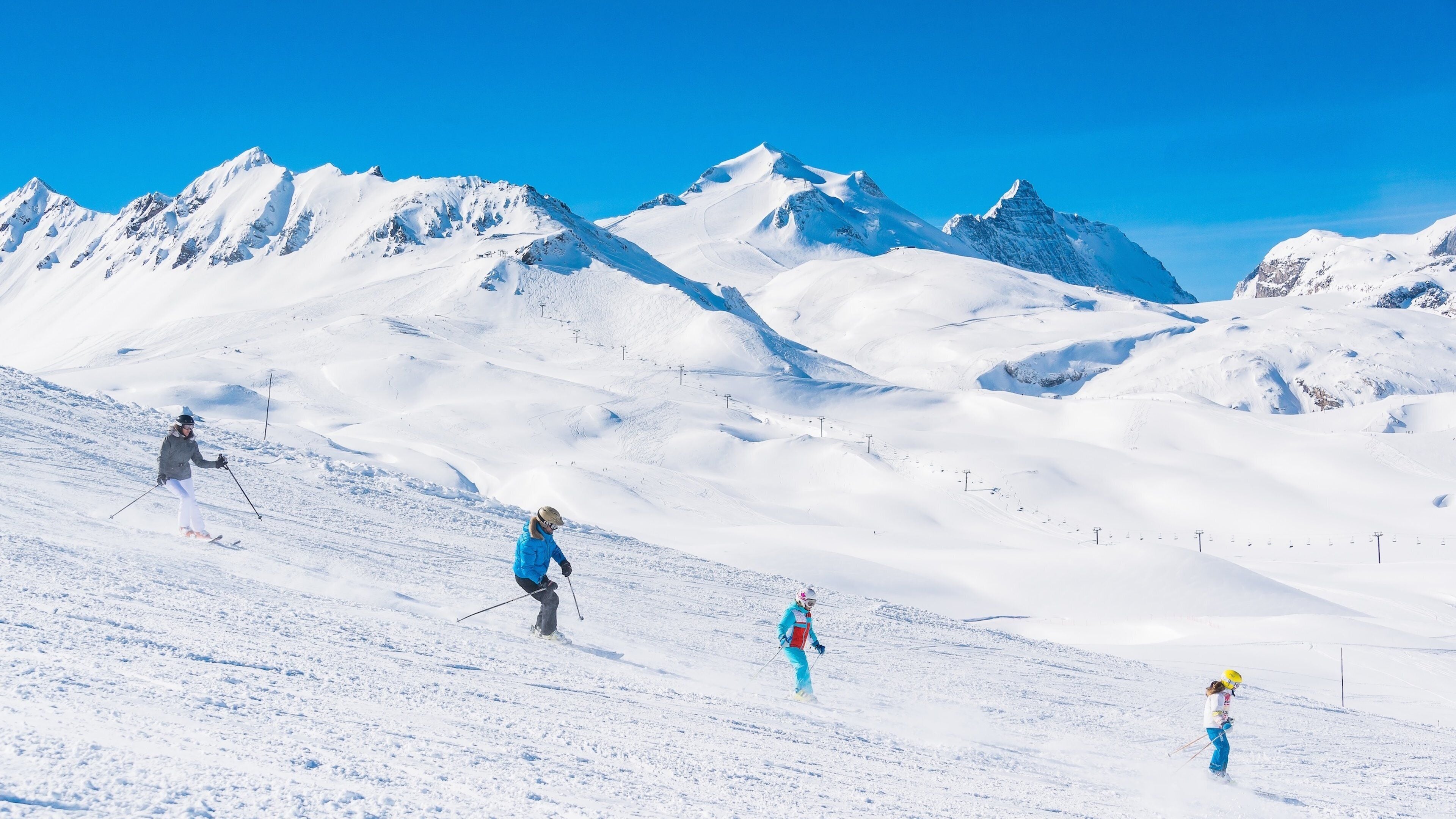 Une pente de montagne enneigée, avec des skieurs et un ciel bleu dégagé.