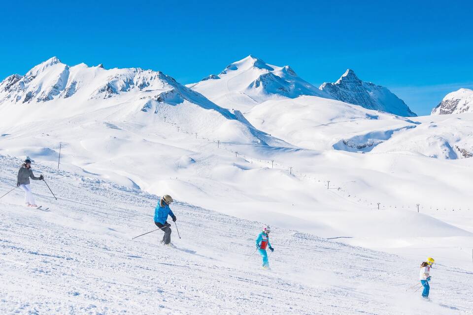 Pendio montuoso innevato con sciatori e un cielo azzurro limpido.