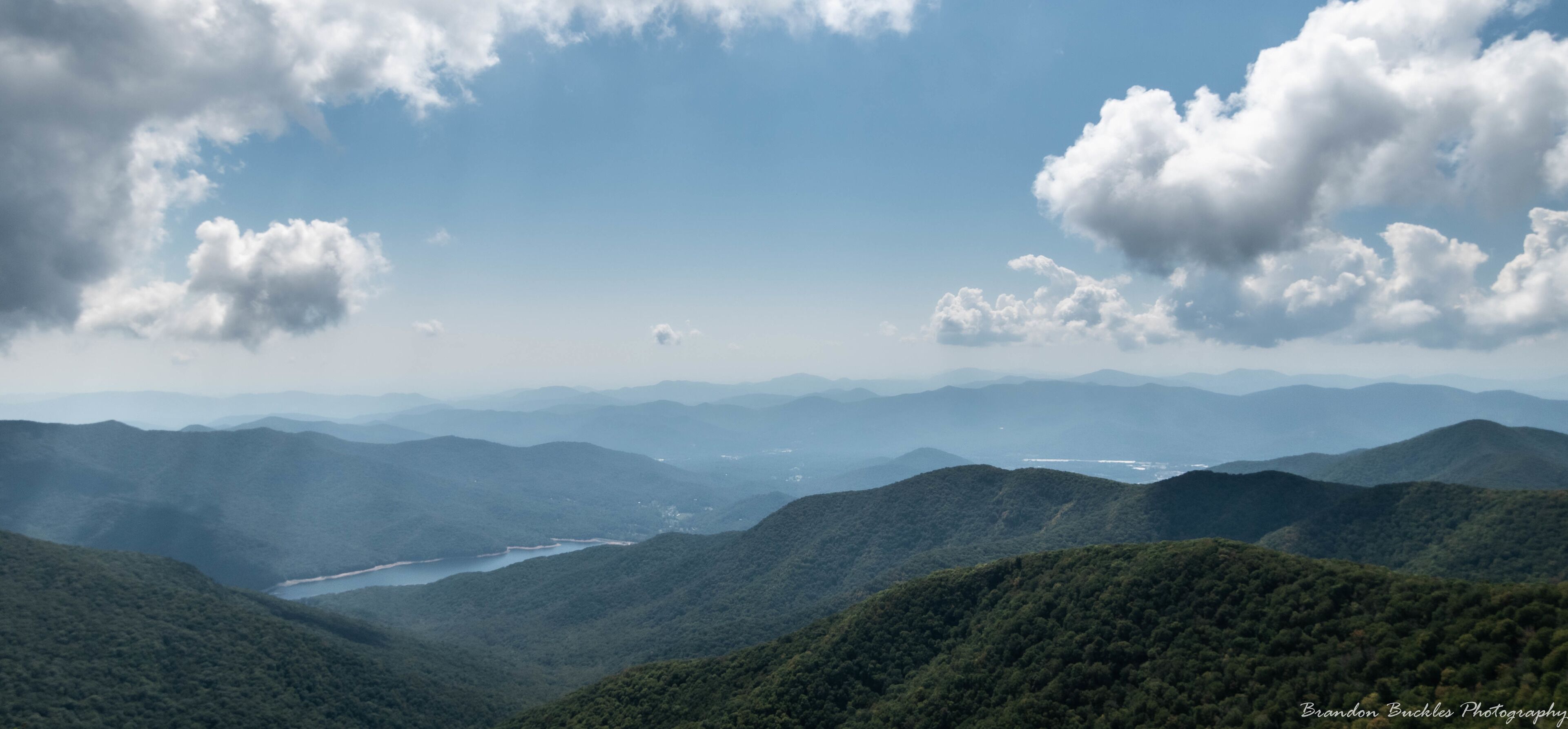 A mountainous landscape with a river and distant mountains under a partly cloudy sky.