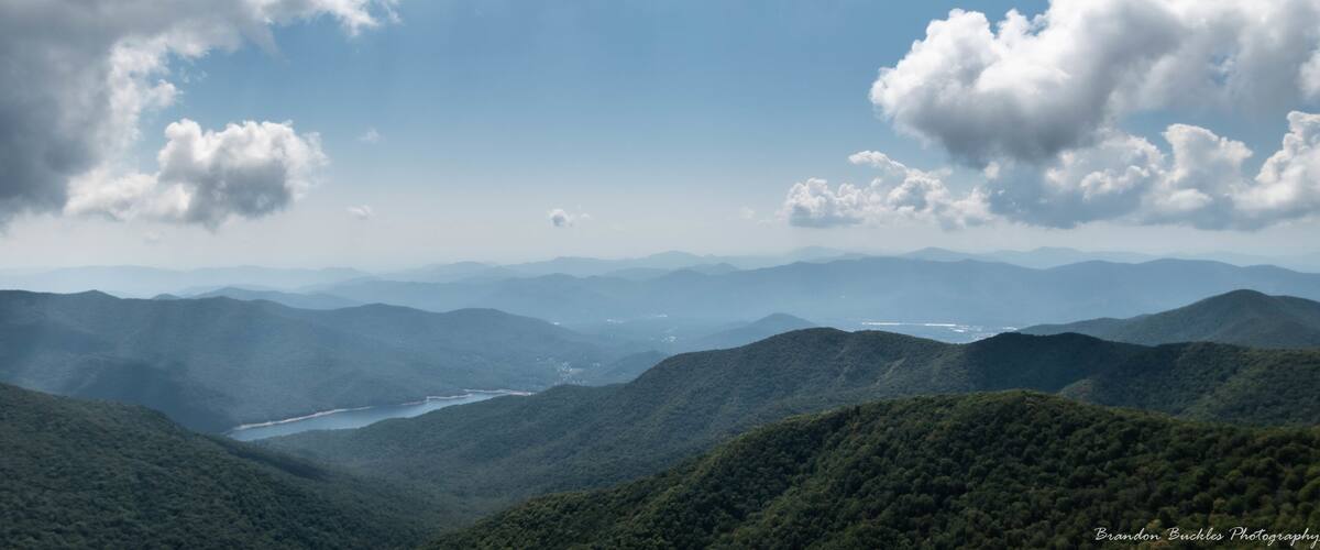 A mountainous landscape with a river and distant mountains under a partly cloudy sky.