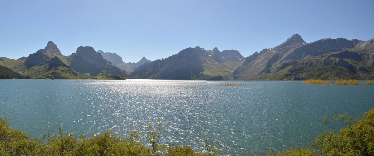 A lake with mountains in the background and a bridge on the left.
