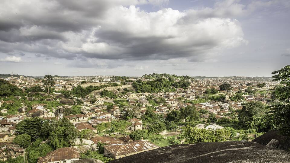 A sprawling cityscape with dense housing, green hills, and a cloudy sky.