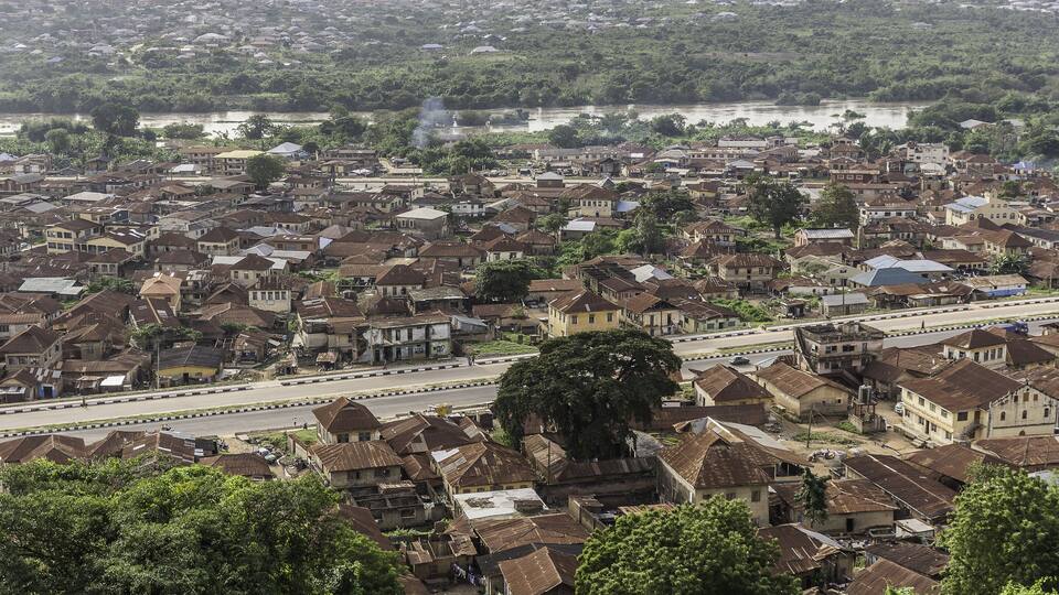 A densely populated urban area with numerous houses, a river in the background, and a large tree in the foreground.