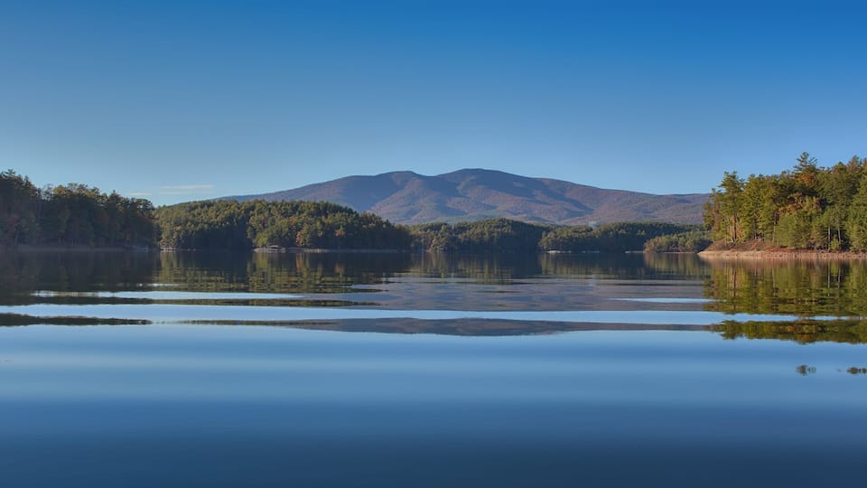 A calm lake with reflections of trees and mountains.