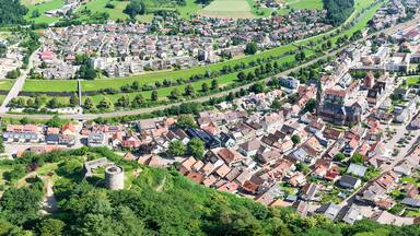 An aerial view of a densely populated town with a mix of residential buildings, a prominent castle, and surrounding green fields.