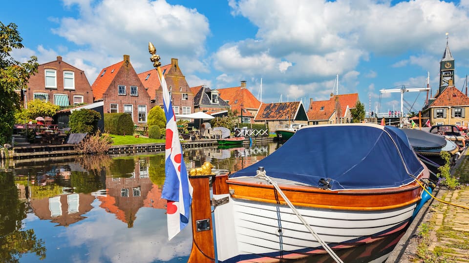 A canal with a boat docked, traditional buildings, and a church steeple.