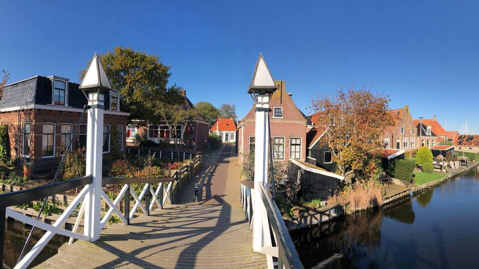 A canal with a wooden bridge, traditional buildings, and a clear blue sky.