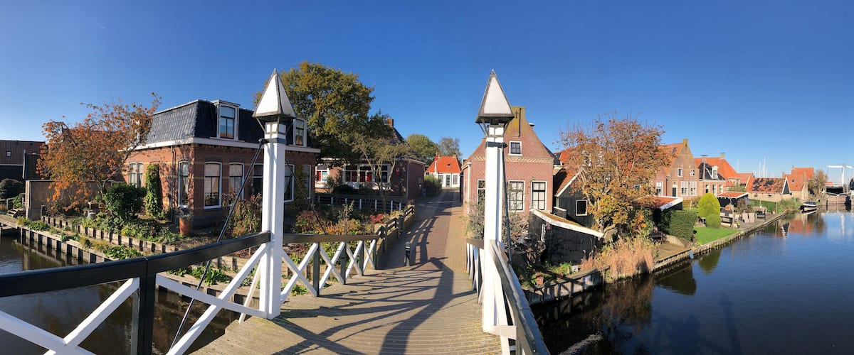 A canal with a wooden bridge, traditional buildings, and a clear blue sky.