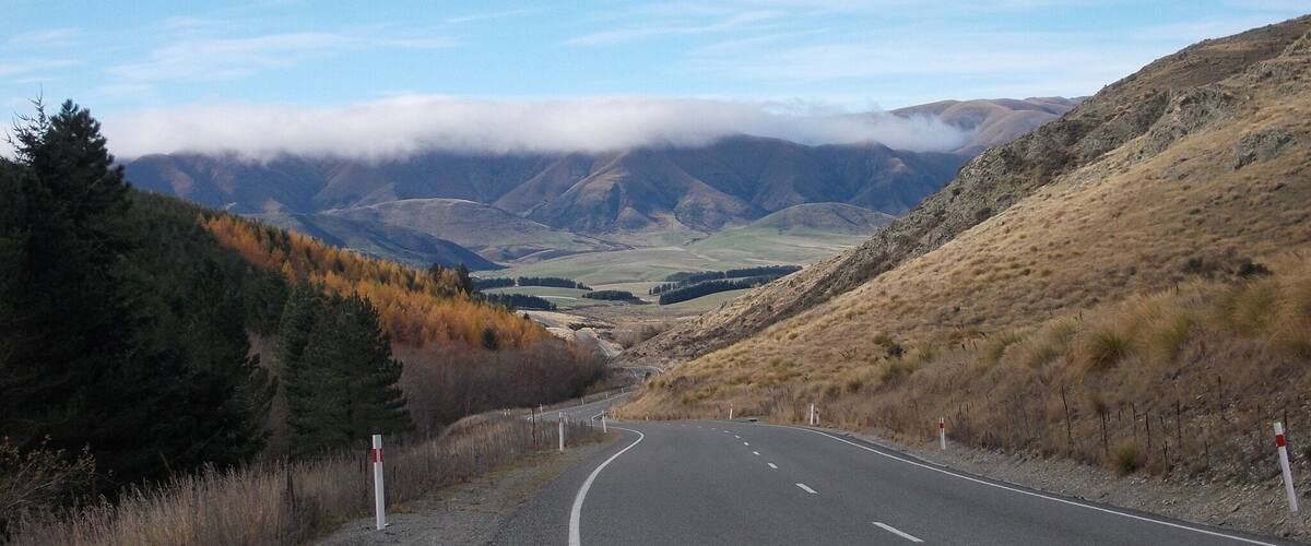 A winding road through a mountainous landscape with autumn-colored trees and a valley in the distance.