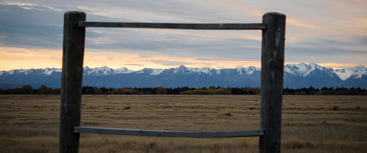 A metal gate in a field with a mountain range in the background.