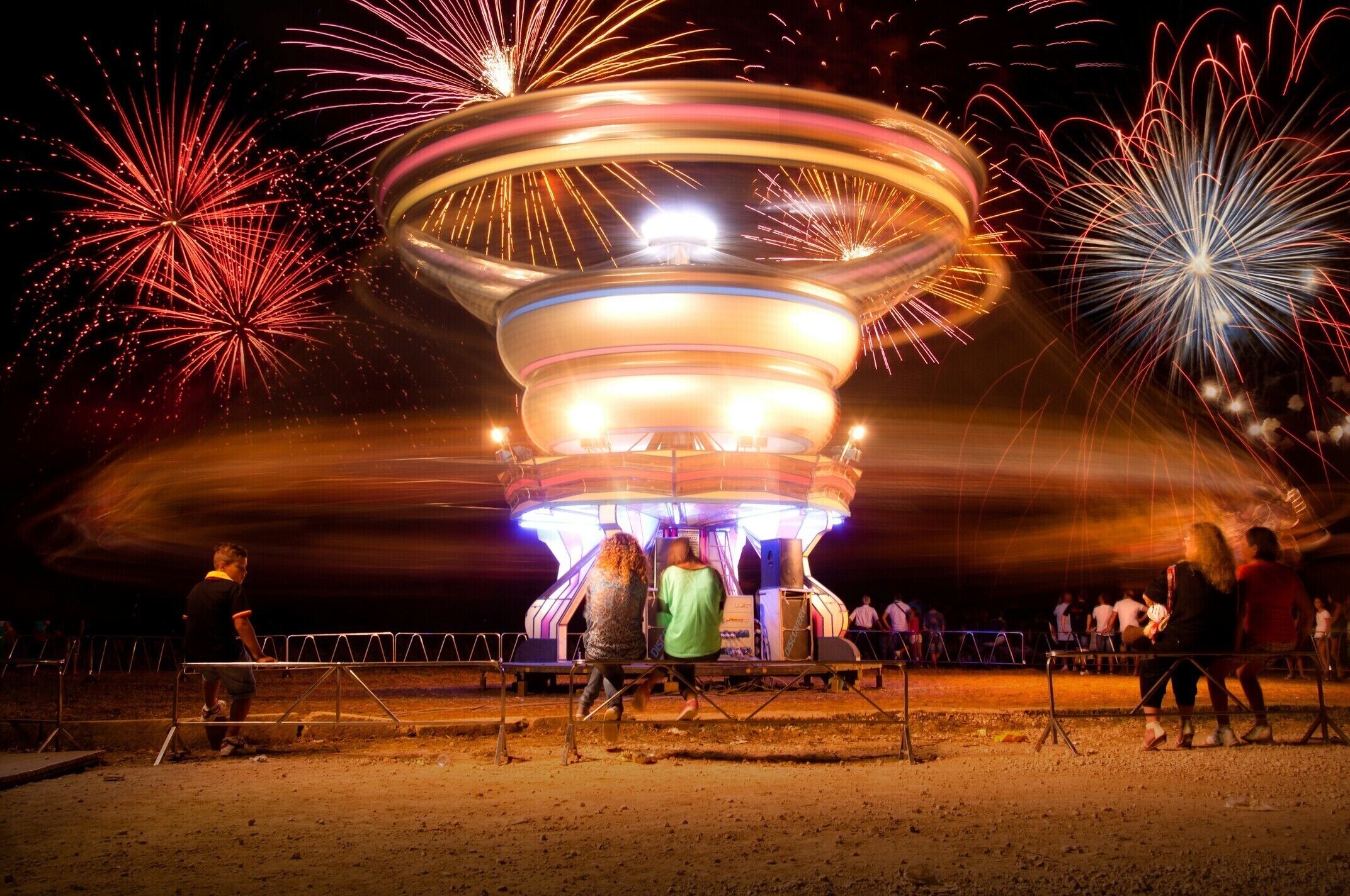 A carousel with colorful lights and fireworks in the background.