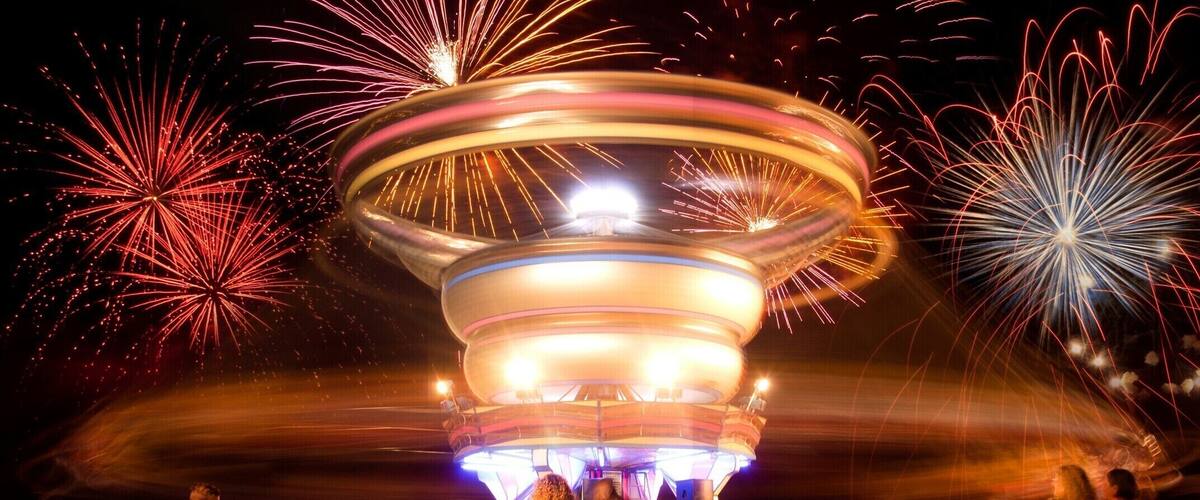 A carousel with colorful lights and fireworks in the background.
