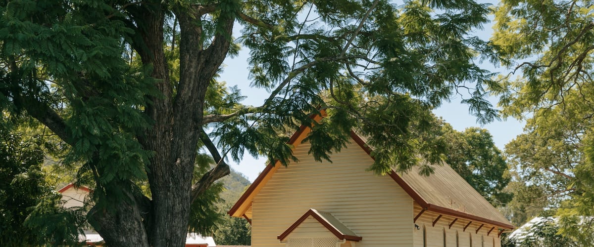 A small wooden church with a sloped roof, surrounded by trees and grass.