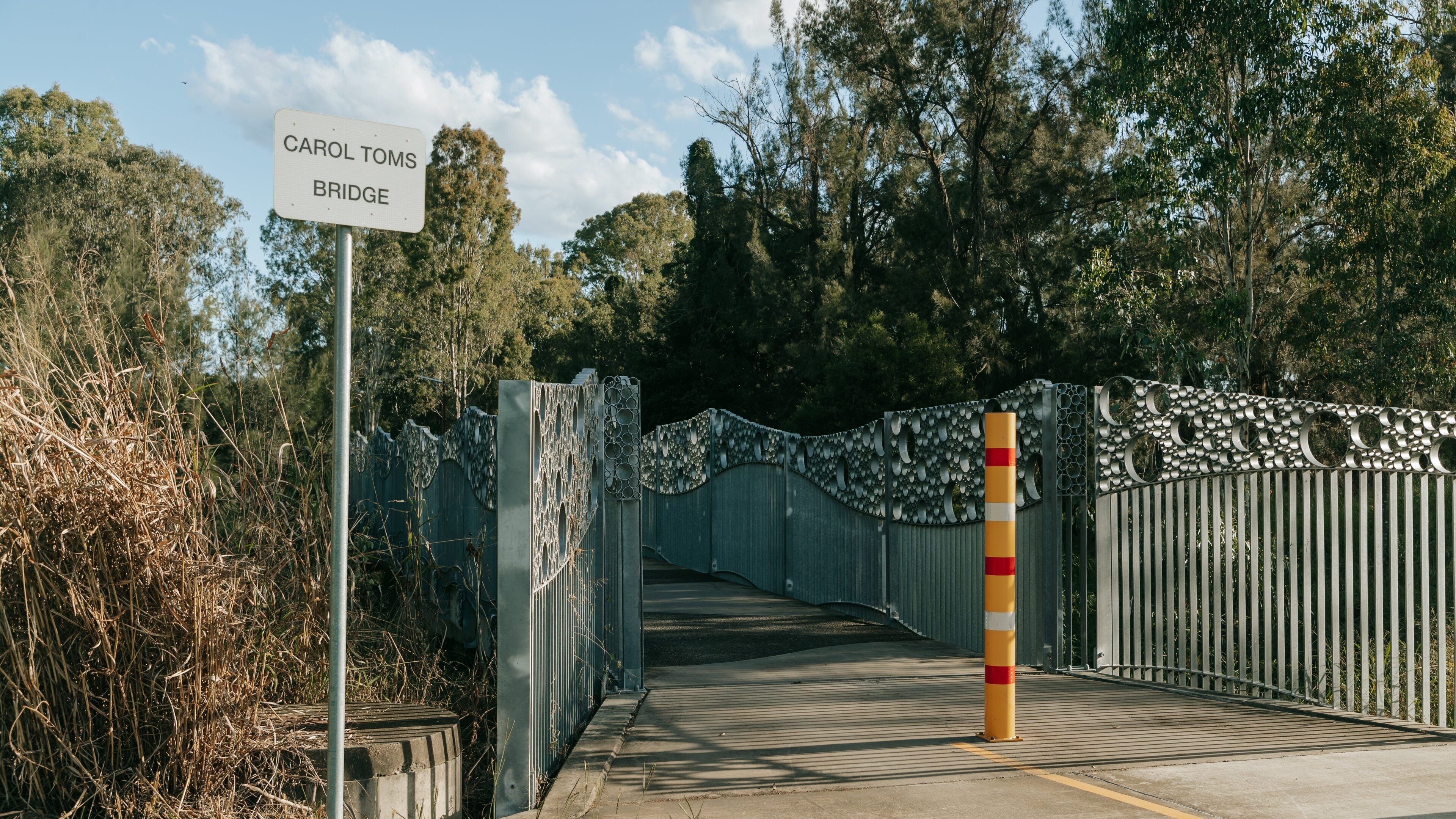 A metal bridge with a decorative fence and a sign that reads "CAROL TOMS BRIDGE".