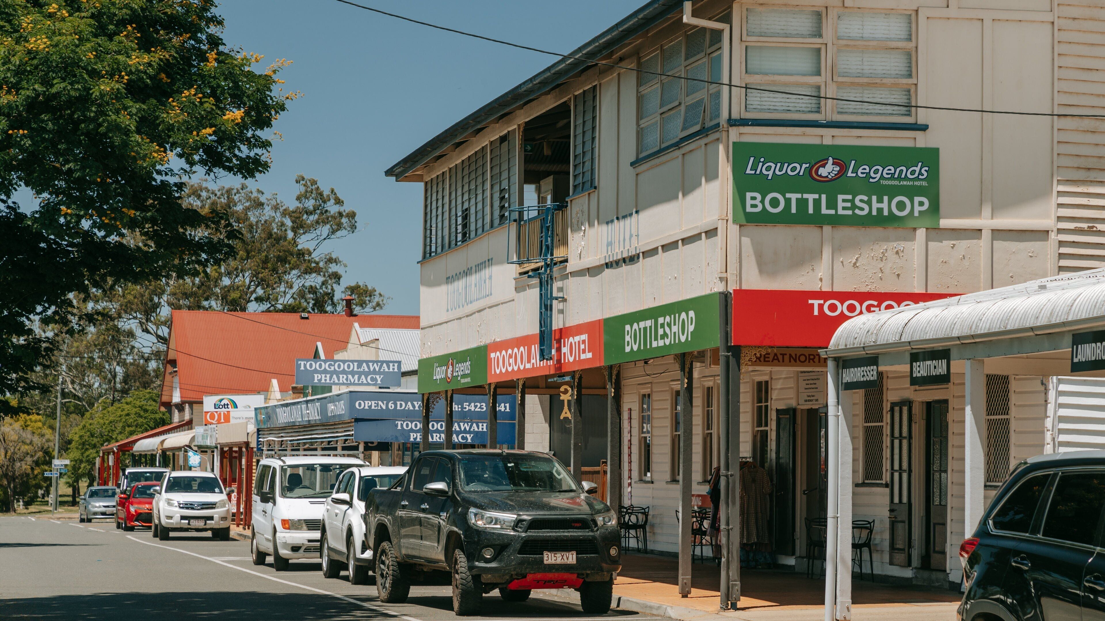 A street with multiple businesses including a liquor legends bottleshop, Toogoolawah pharmacy, and Toogoolawah hotel.
