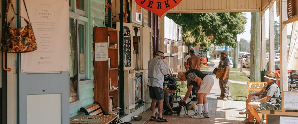 A coffee shop with a red sign reading "Coffee & Jerky". There are people sitting and standing outside, and a dog on a leash.