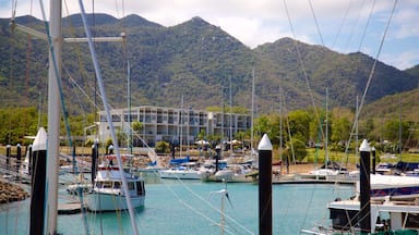 A marina with boats docked, a building with multiple balconies, and a mountainous backdrop.