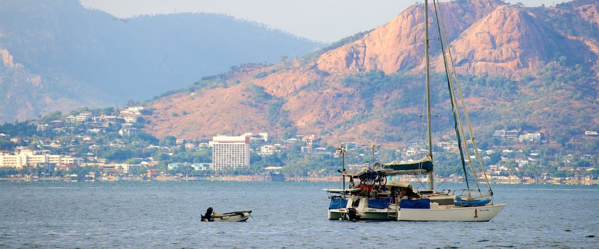 A sailboat on calm waters with a cityscape and mountains in the background.