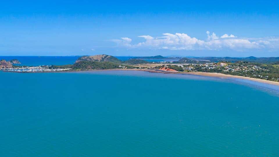 A coastal landscape with a sandy beach, a small island with rocky outcrops, and a town with houses and buildings.