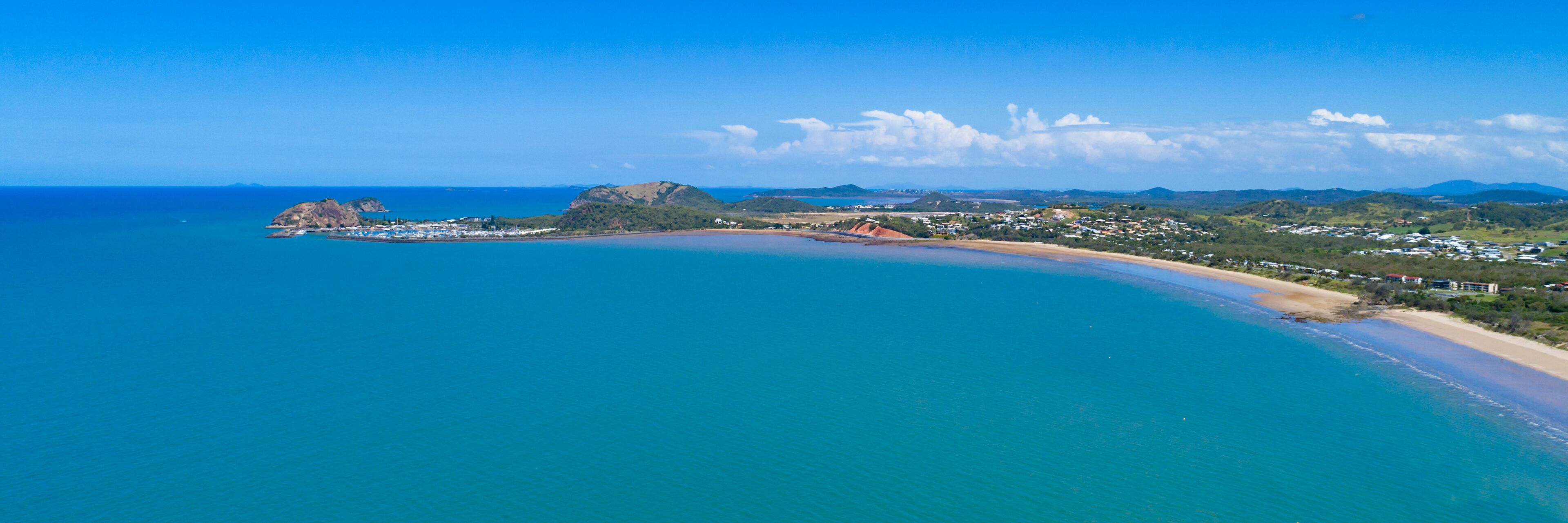 A coastal landscape with a sandy beach, a small island with rocky outcrops, and a town with houses and buildings.
