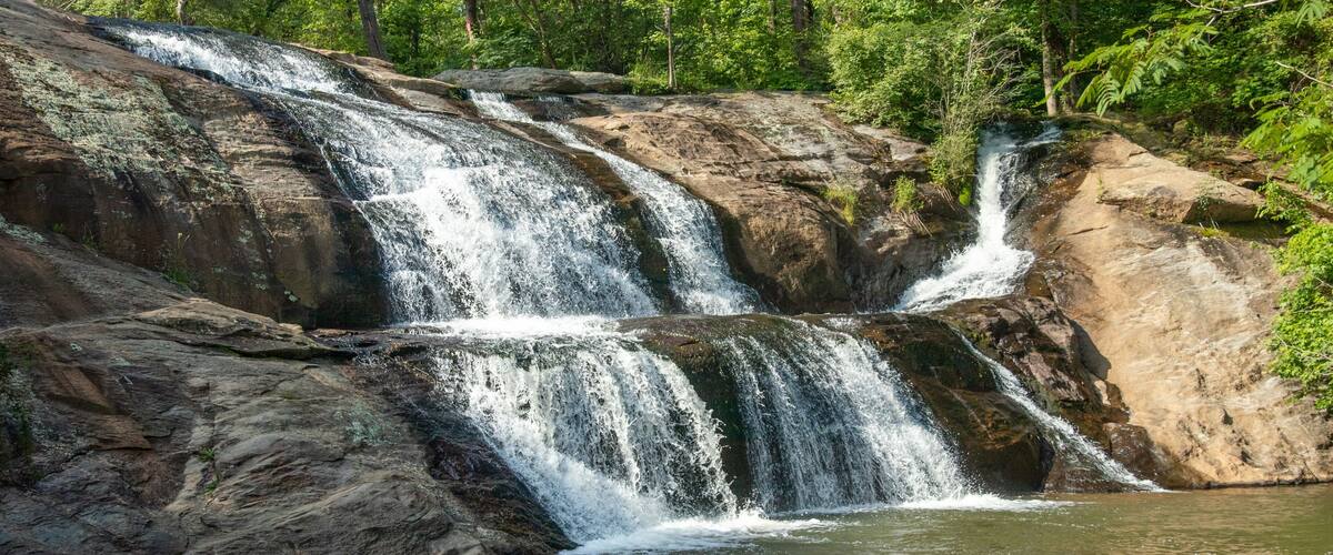A multi-tiered waterfall surrounded by dense forest.