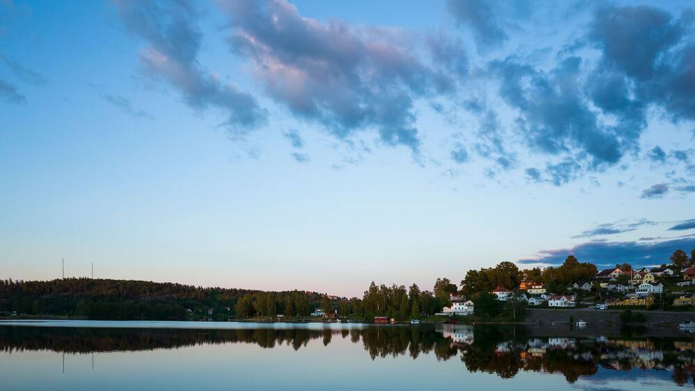 Bengtsfors city by the Lelång lake at Swedish summer night, Nordic town reflecting in calm water at blue hour, Sweden