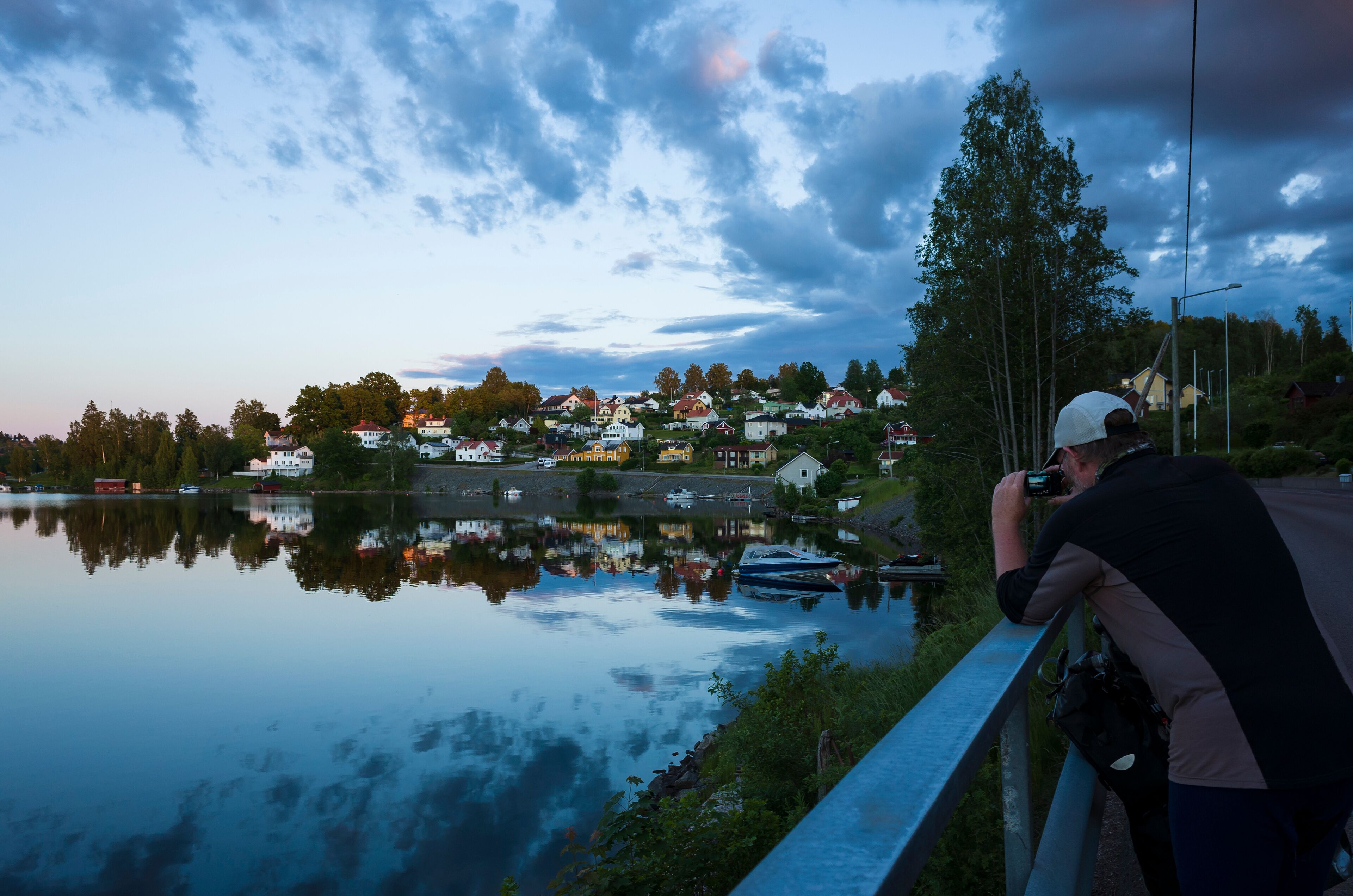 Bengtsfors city by the Lelång lake at Swedish summer night, Man is photographing city view reflecting in calm water, Sweden