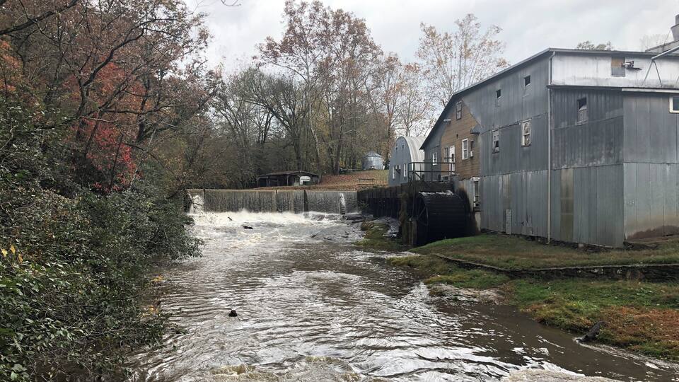 A river flowing through a rural area with a water mill and a small building.