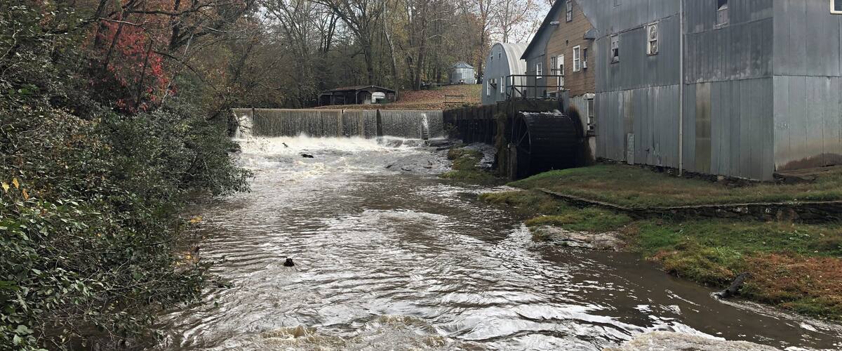 A river flowing through a rural area with a water mill and a small building.