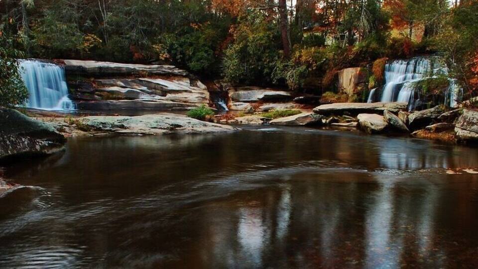 A waterfall cascading over rocks into a calm pool surrounded by autumn foliage.