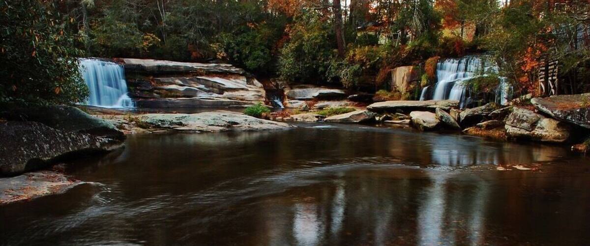 A waterfall cascading over rocks into a calm pool surrounded by autumn foliage.