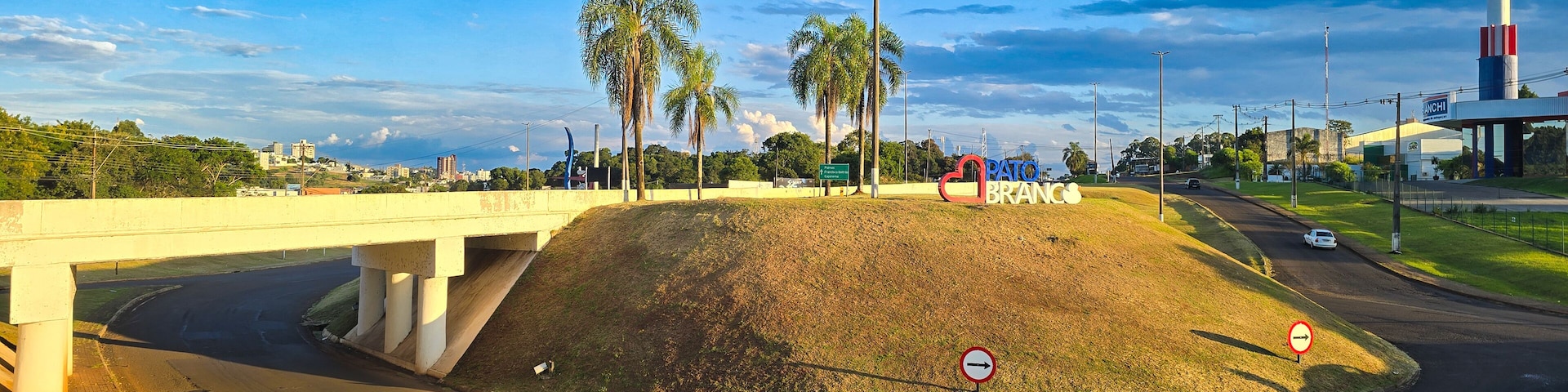 Uma rotatória com palmeiras, uma ponte e uma placa indicando "Pato Branc's".