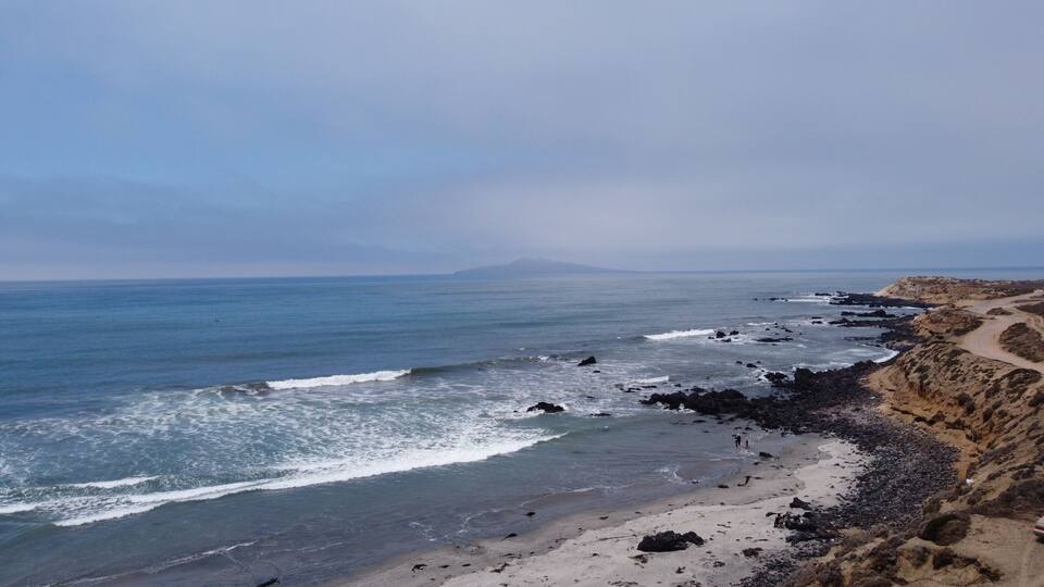 A coastal landscape with a rocky shoreline, a sandy beach, and a distant mountain.